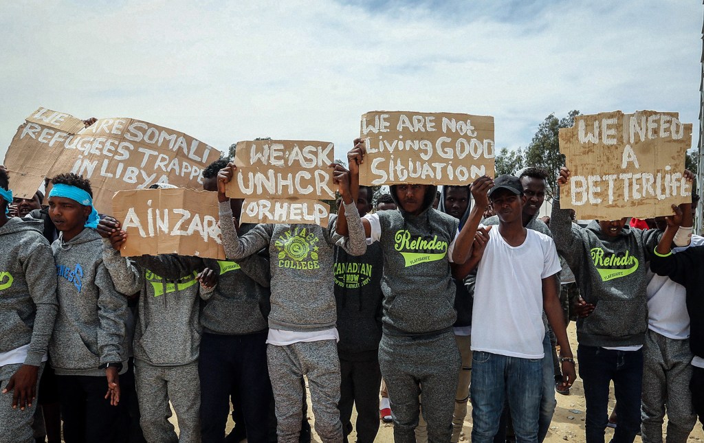 Un grupo de migrantes sostienen pancartas durante la visita del secretario general de las Naciones Unidas, Antonio Guterres, al centro de detención de migrantes de Ain Zara, en Trípoli, el 4 de abril de 2019. (Foto: Mahmud Turkia/AFP vía Getty Images)